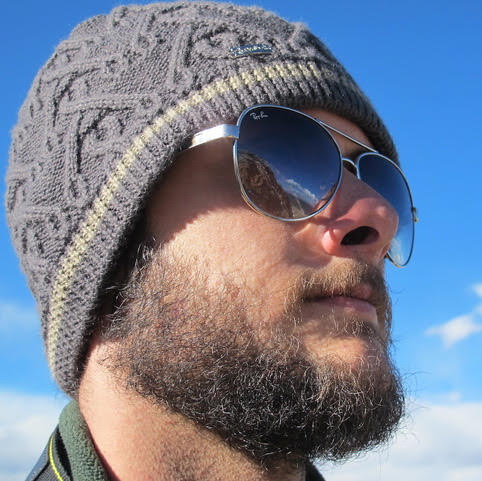 Close-up portrait of a bearded man in a knit hat and sunglasses