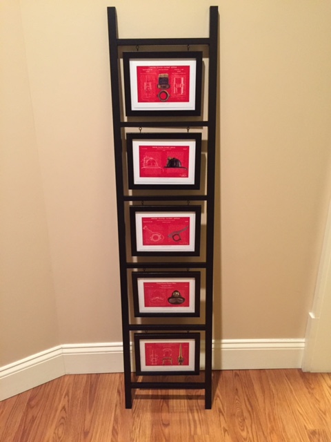 Five small red patent prints stacked in a tall black ladder frame